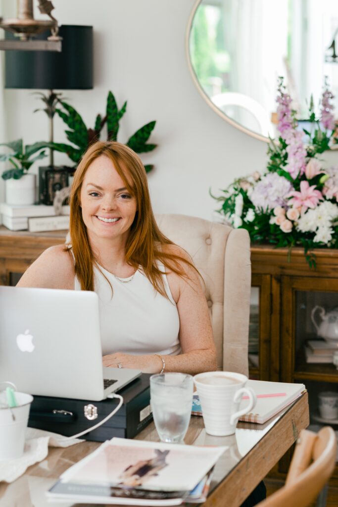 Christine Coughlin sits behind her laptop smiling at the camera as she prepares to host the Rise and Monetize Creators Summit