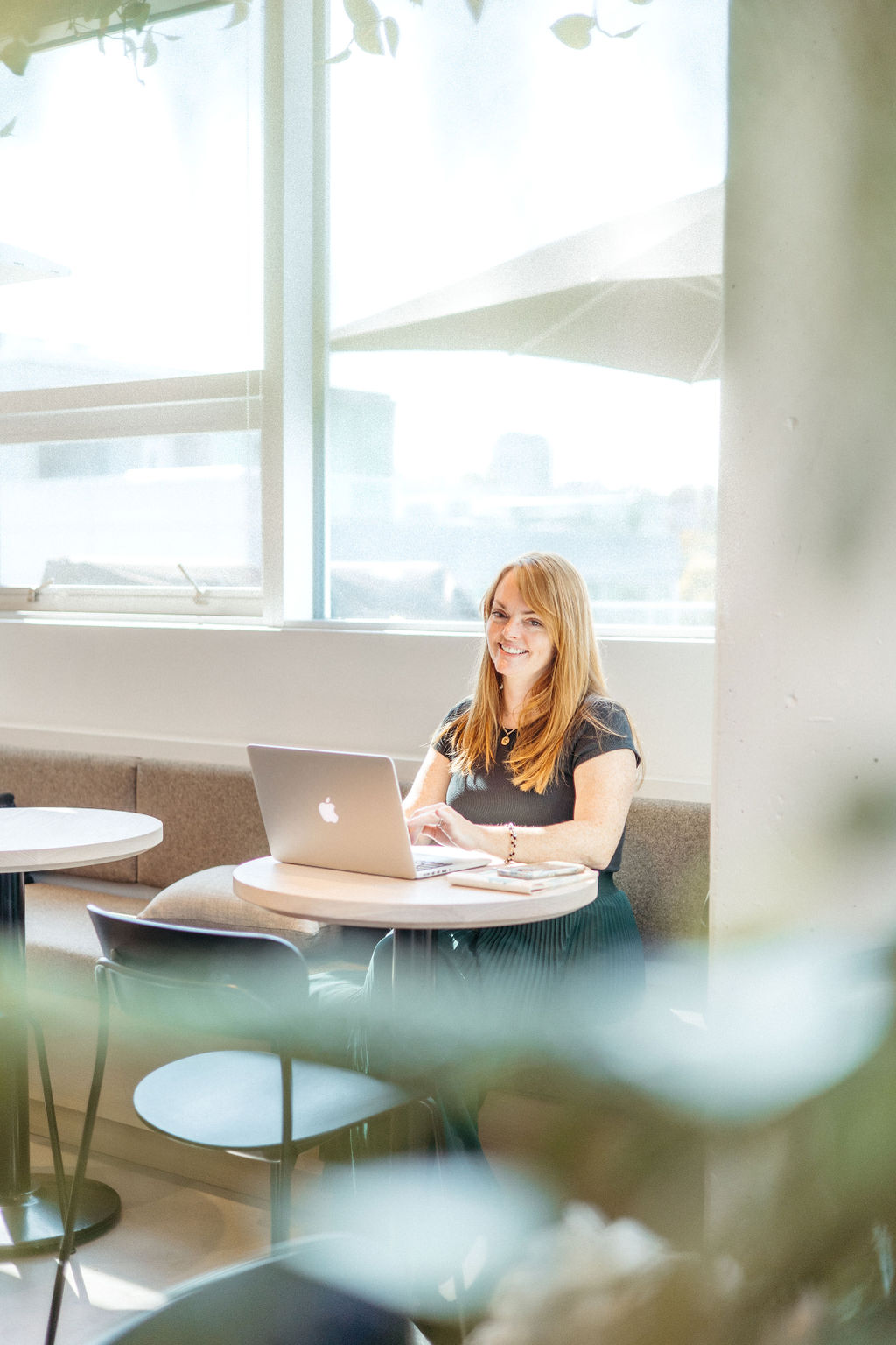 Christine coughlin sits in a cafe with her laptop smiling at the camera.